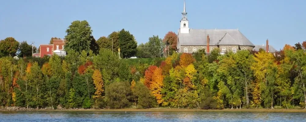 Saint-Pierre-les-Becquets seen from the river: the church spire, the autumn maples and the shore.